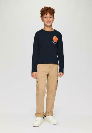 Marineblauwe long-sleeve shirt met een oranje basketbalafbeelding, gecombineerd met beige cargobroek en witte sneakers met een zwarte accenten.