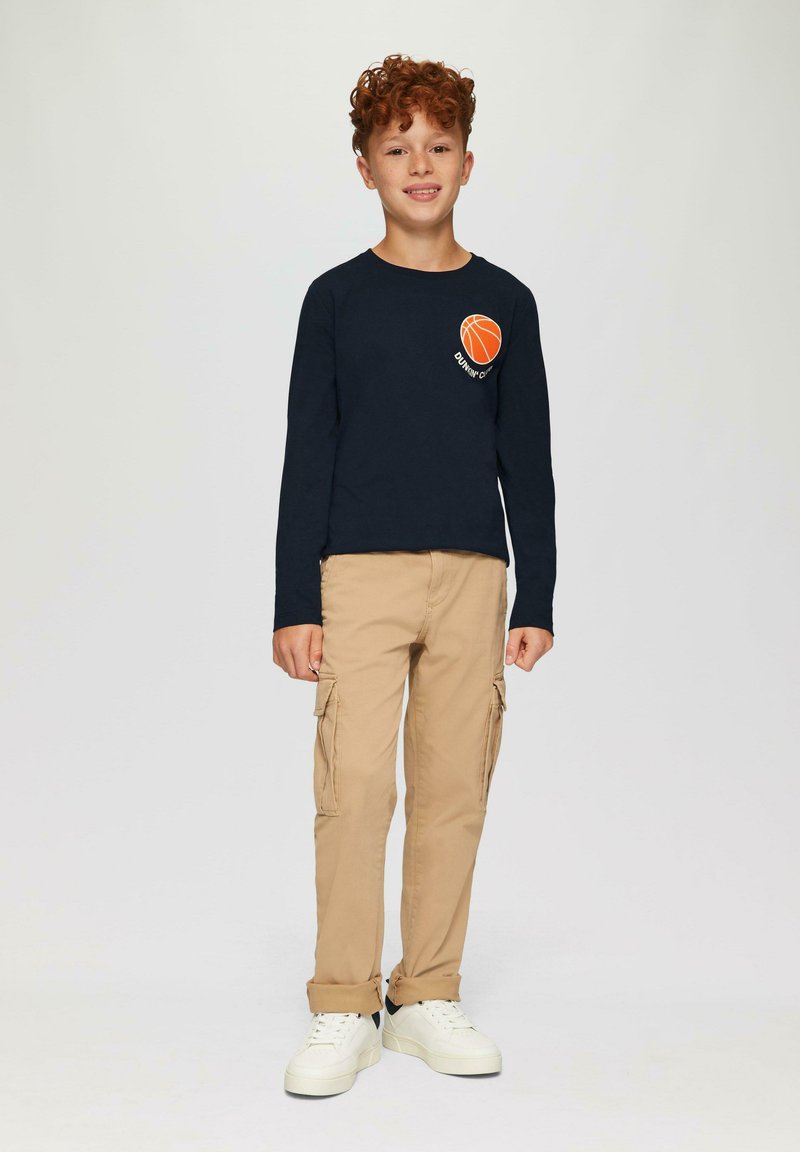 Marineblauwe long-sleeve shirt met een oranje basketbalafbeelding, gecombineerd met beige cargobroek en witte sneakers met een zwarte accenten.