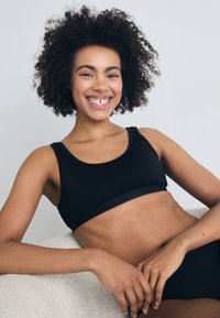 Čierny rebrovaný crop top so širokým pásom a vlnkovanými okrajmi, s uvoľneným strihom. Hladká textúra, doplnená minimalističným dizajnom.