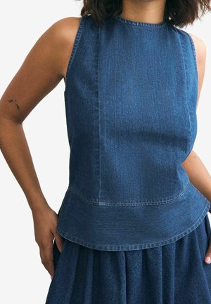 Ærmeløs mørkeblå denimtop med rund halsudskæring og lagdelt kant båret af en person med en lille tatovering på venstre overarm.