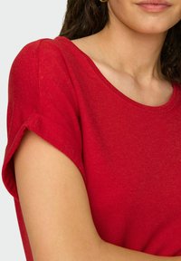 Czerwona koszula krótki rękaw z miękkiego materiału, z lekko okrągłym dekoltem i subtelną fakturą. Podwinięte rękawy dodają szczegółu.