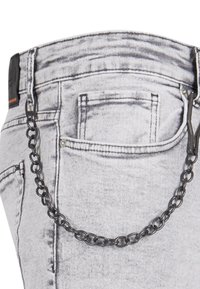 Jean en denim gris avec une finition texturée, arborant un accent en chaîne noire fixé à la poche arrière, mis en valeur par de subtils détails de couture.