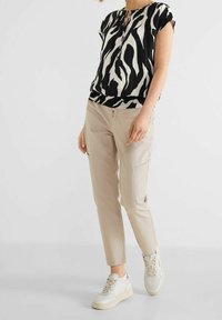 Kurzärmelige Bluse im Schwarz-Weiß-Zebra-Print, kombiniert mit hellbeigen Hosen. Die Sneaker sind weiß mit grauen Akzenten. Weicher Stoff, lässige Passform.