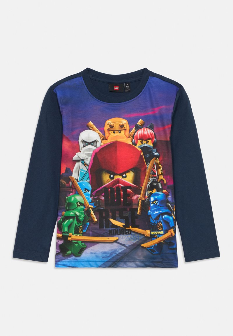 Garās piedurknes tumši zilā T-krekls ar krāsainu LEGO ninju grafiku, uz kuras redzams uzraksts "We Rise", pret spilgtu fona. Mīksta kokvilnas auduma.