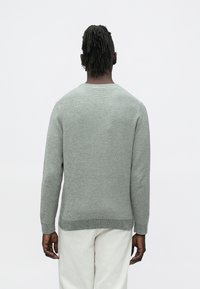 Szürke kötött pulóver hosszú ujjakkal és kerek nyakkivágással, texturált mintával. Az alja és a mandzsettái bordázottak a kényelmes illeszkedés érdekében.