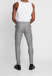 Šedé kostkované slim-fit kalhoty s plochým předkem, poutky na opasek a zadní kapsou, spolu s bílým tílkem a černými botami.