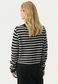Striped sweater in navy and cream, featuring a ribbed neckline and cuffs. Knitted texture with a cropped design, worn with a dark, textured skirt.