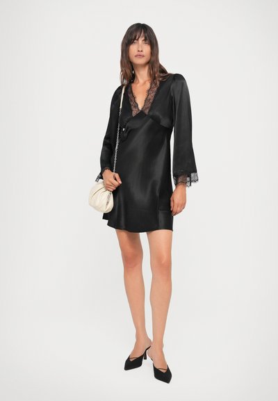 Black satin dress with long sleeves, V-neckline, and lace trim. Paired with pointed-toe black heels and a cream colored handbag.
