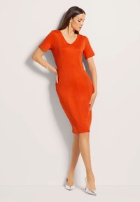 Rode aansluitende jurk met korte mouwen, V-hals en naaddetails. Gekoombineerd met zilveren puntige hakken. Soepele stof en knielange pasvorm.
