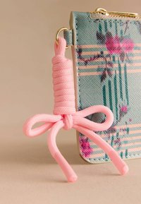 Maksts ar ziedu rakstu zilgani zaļā krāsā un rozā akcentiem. Tai ir rozā auklas vilkšanas mezgls lokā, kas piešķir struktūru un detaļas. Iekļautas zelta mēbeļu detaļas.