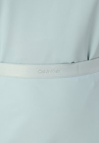 Svetlo modra obleka z gladko teksturo, ki ima ujemajoč pas in subtilni embosirani logotip Calvin Klein. Preprosta zasnova, brez vzorcev.