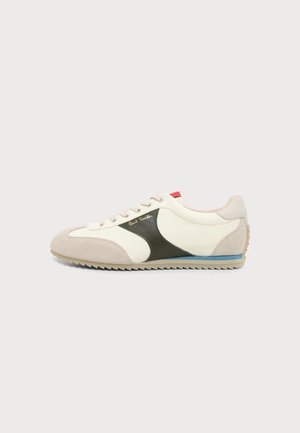 Baskets beige et blanches à profil bas avec détail latéral noir, lacets à l'avant, languette de talon rouge et bande bleue sur la semelle.