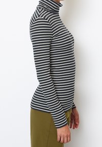 Stribet turtleneck bluse i navy og creme, ribbet tekstur, slim fit, med lange ærmer og høj halsudskæring, parret med olivengrønne bukser.