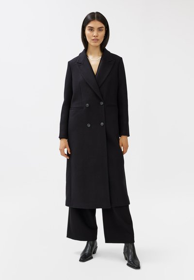 Cappotto doppiopetto nero con grandi bottoni, design sartoriale, lunghezza lunga e revers a punta, realizzato in tessuto di lana testurizzata.