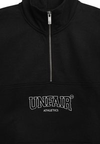 Svart zip-up genser laget av mykt stoff, med høy krage og hvit brodert tekst "UNFAIR ATHLETICS" på forsiden.