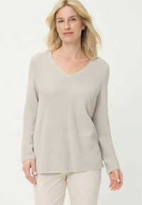 Beige pullovertrui met wafeltjesstructuur, een V-hals, lange mouwen en een losse pasvorm. Geribbelde boorden en zoom zorgen voor textuur.