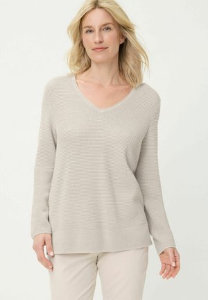 Beige pullovertrui met wafeltjesstructuur, een V-hals, lange mouwen en een losse pasvorm. Geribbelde boorden en zoom zorgen voor textuur.