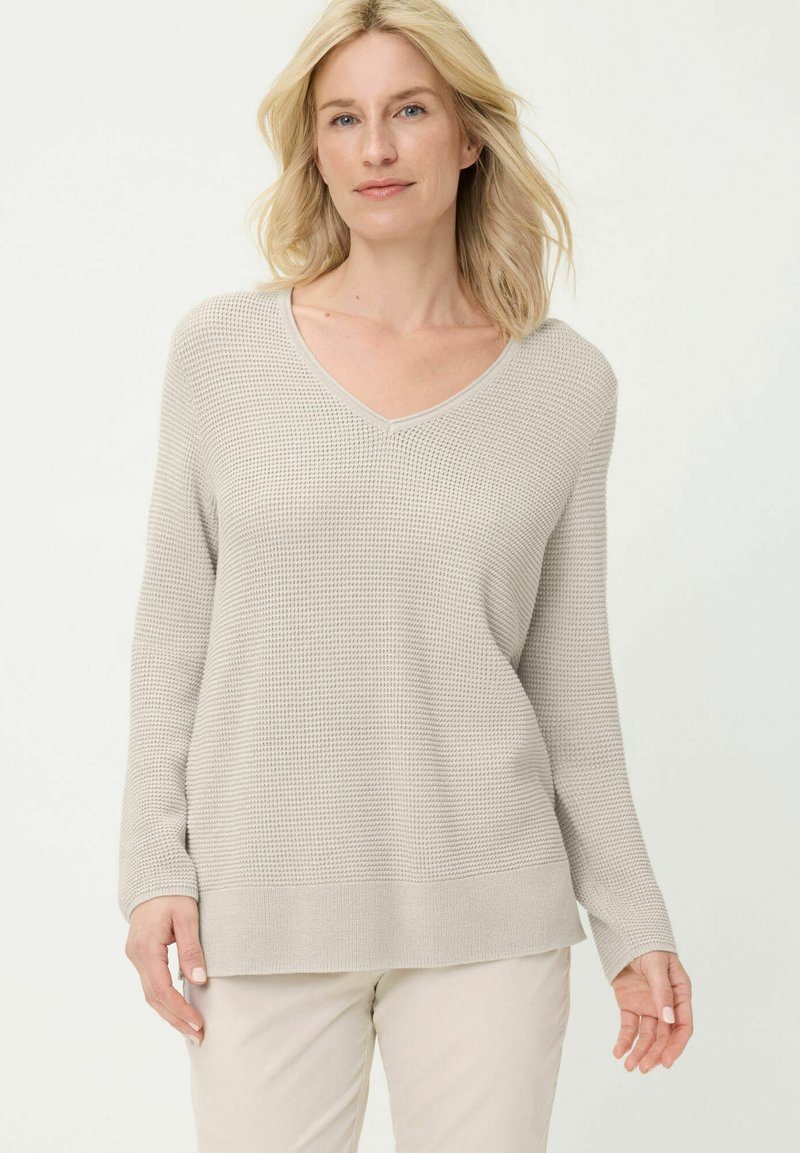 Beige pullovertrui met wafeltjesstructuur, een V-hals, lange mouwen en een losse pasvorm. Geribbelde boorden en zoom zorgen voor textuur.