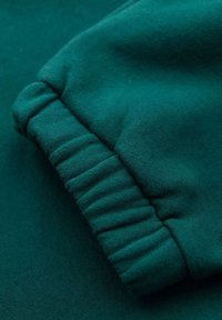 Tela de sudadera verde con detalle de puños acanalados. La textura es suave y lisa, con un acabado ligeramente elástico.