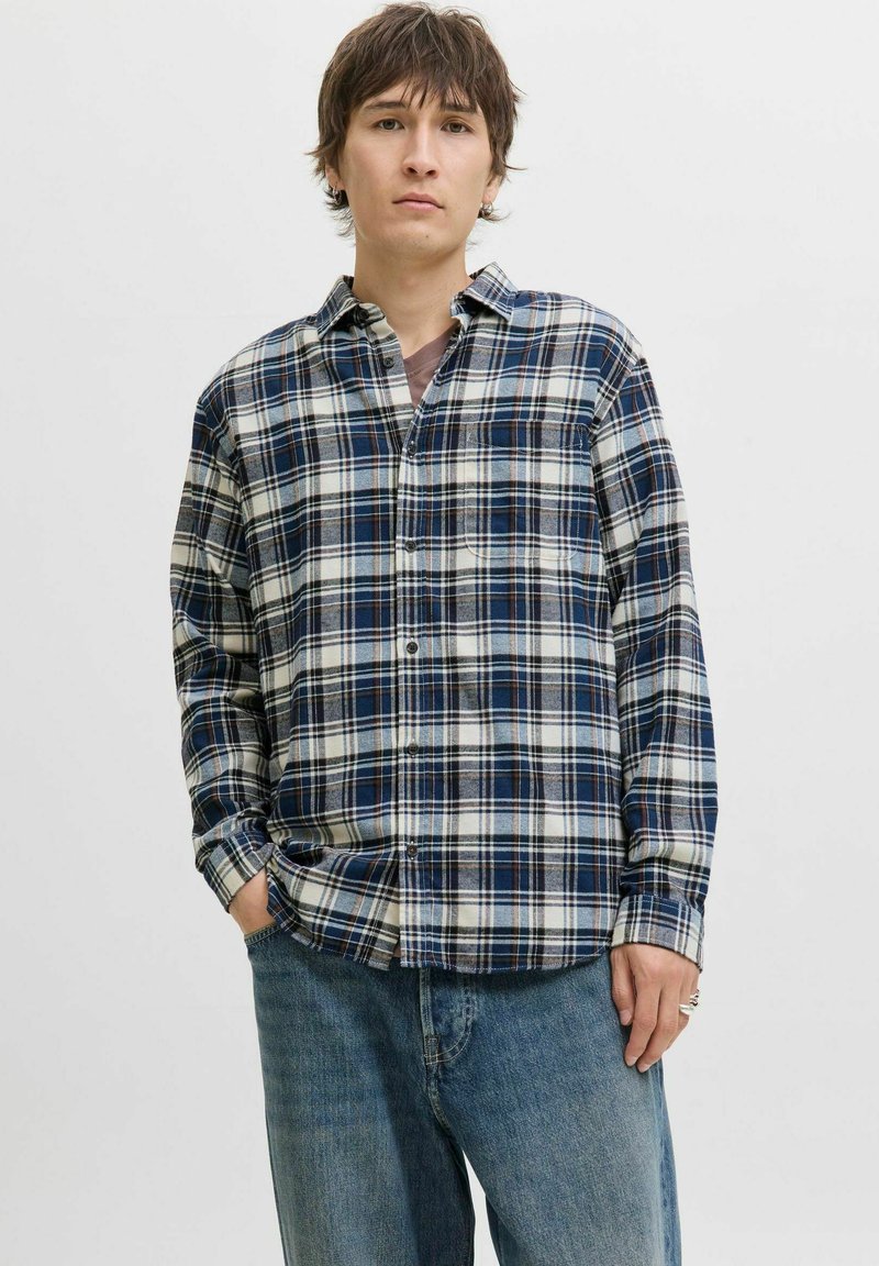 Rutet skjorte i blå, hvid og mørke nuancer; lange ærmer, knap-åben krave, brystlomme, afslappet pasform, struktureret stof. Bæres med blå jeans.