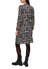 Leopardenmuster-Kleid in Grautönen, mit taillierter Taille, langen Ärmeln und einem mehrlagigen Rüschensrock. Kombiniert mit schwarzen Knöchelstiefeln.