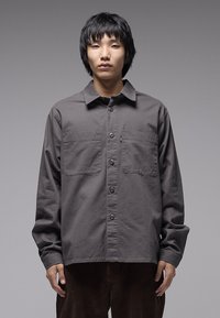 Γκρι πουκάμισο με κουμπιά από βαμβάκι, με δύο τσέπες στο στήθος, μακριά μανίκια και άνετη εφαρμογή. Διακριτική υφή με λείο φινίρισμα.