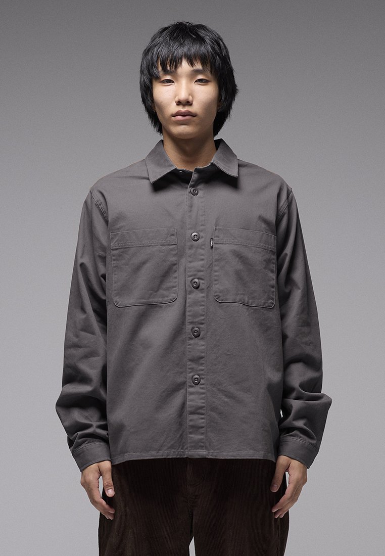 Γκρι πουκάμισο με κουμπιά από βαμβάκι, με δύο τσέπες στο στήθος, μακριά μανίκια και άνετη εφαρμογή. Διακριτική υφή με λείο φινίρισμα.
