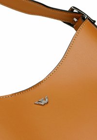 Borsa in pelle color caramello con una superficie liscia, design curvato e logo argentato. Presenta un bordo cucito e una tracolla regolabile.