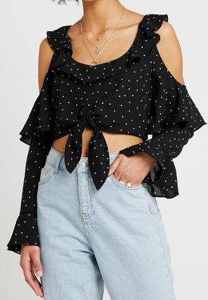Crop top noir à pois blancs, épaules dénudées, manches à volants, nœud sur le devant, associé à un jean taille haute bleu clair.