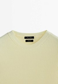 Ribbed cream sweater with a round neckline. Label features black text on a white background. Soft texture and lightweight material.