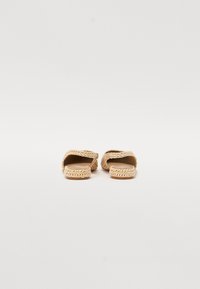 Pīts salmu sandales ar atvērtu purngalu un aizmuguri, plakanā zole un gaiši bēša krāsa; dabīgā tekstūra ar woven detaļām.