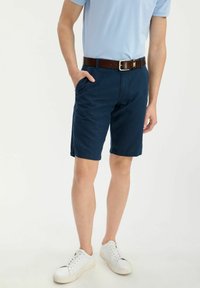 Granatowe szorty wykonane z bawełny o prostym kroju, z dwoma kieszeniami po bokach. Połączone z jasnoniebieską koszulą i białymi trampkami.