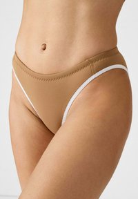 Bas de bikini couleur sable avec une coupe taille basse, présentant des coutures blanches le long des bords, une texture lisse et un design simple sans motifs.