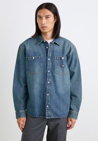 Denimskjorte i medium blå med to brystlommer, knaplukning foran og klassisk krave. Har lys fading og en robust tekstur.
