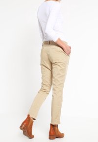 Pantalon beige slim fit avec poches latérales, présentant une texture douce et une taille élastique. Associé à des bottes cheville marron, mettant en avant un design épuré.