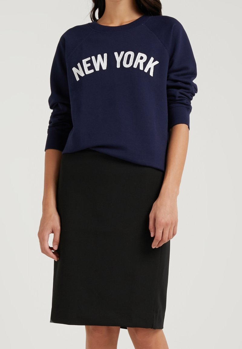 Sweat-shirt bleu marine avec lettrage blanc « NEW YORK », associé à une jupe noire ajustée. Le tissu semble lisse avec un design décontracté.
