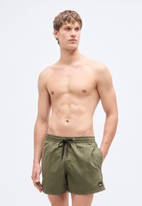 Πράσινα μαγιό με κορδόνι στη μέση, φτιαγμένα από απαλό ύφασμα, με μικρό λογότυπο στην κάτω αριστερή πλευρά.