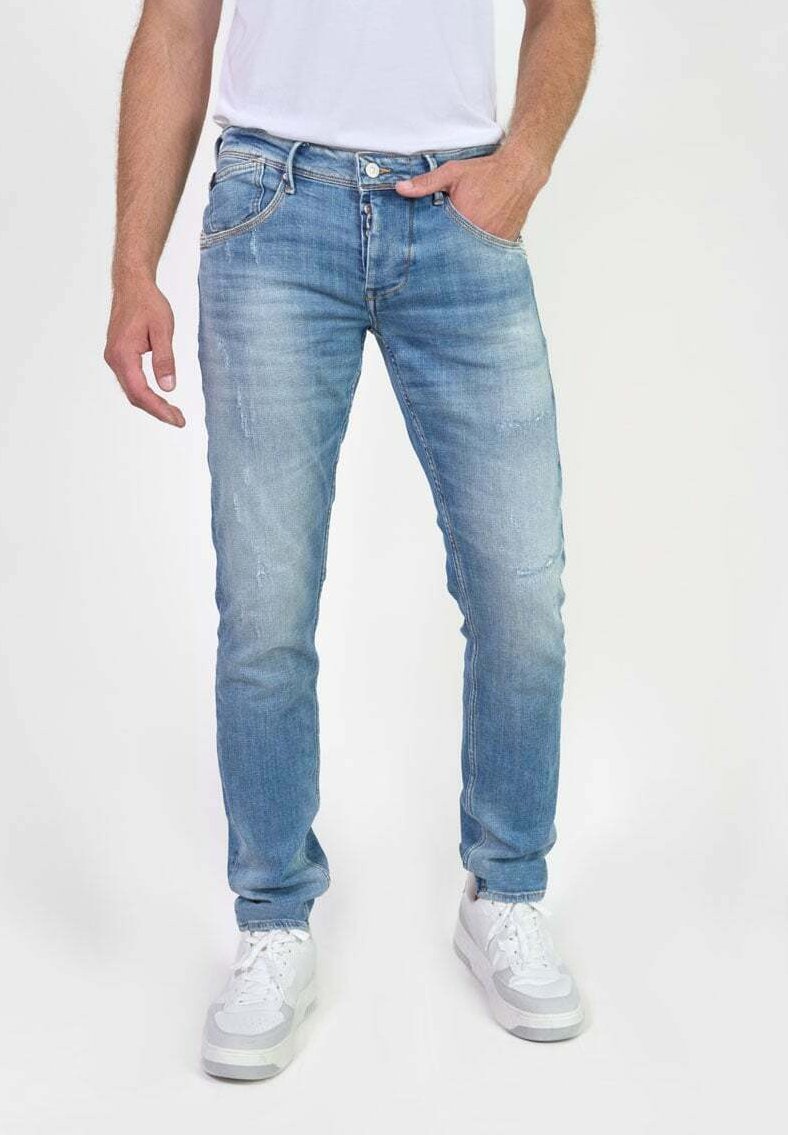 Pantalones vaqueros de mezclilla azul claro con corte slim, que presentan bolsillos frontales, una textura desgastada y costuras en contraste, combinados con zapatillas blancas.