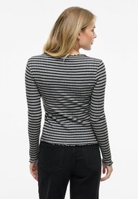 Långärmad, åtsittande topp i grå och svarta vertikala ränder; ribbad textur med vågiga scallopdetaljer vid halsen och nederkanten.