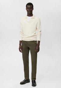 Cream ribbed knit pullover with a wide collar, paired with olive green tapered trousers and black slip-on shoes. Simple and modern design.