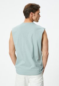Camiseta sin mangas de color azul claro con cuello redondo, hecha de una tela suave, que presenta un corte relajado y un diseño sencillo. Sin patrones ni acentos visibles.