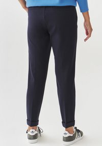 Pantaloni navy con vestibilità affusolata, orlo con risvolto e tasche laterali, abbinati a sneakers grigie e bianche con strisce nere.