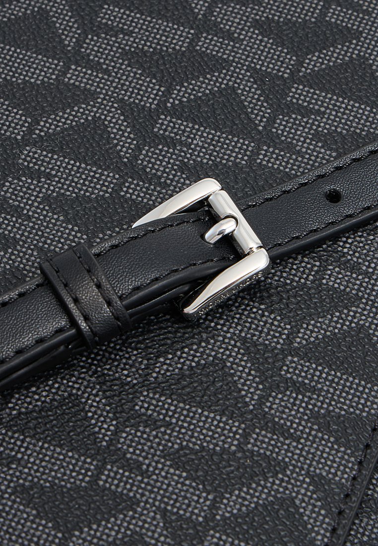 Surface noire à motifs avec un design géométrique, présentant une boucle en argent élégante et une sangle en cuir texturée. Des accents de couture sont visibles.