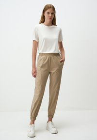 Beige joggingsbroek met elastische tailleband, taps toelopende pijpen, zijzakken en ribgebreide boorden. Gepaard met een effen witte t-shirt met korte mouwen.