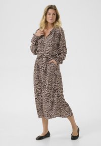 Robe à imprimé léopard avec des manches longues, un col froncé, une ceinture et des poches. Le tissu présente une texture douce dans des teintes de beige et de marron.