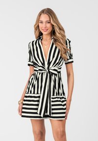 Abito a righe con una combinazione di colori bianco e nero, maniche corte, scollatura a V, fronte annodato e parte inferiore svasata con tasche.