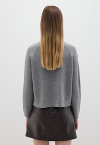 Grau gestrickter Pullover mit einem cropped Design und geripptem Saum, kombiniert mit einem schwarzen Leder-Minirock. Die Textur wirkt weich und glatt.