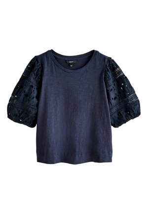 Tengerészkék rövid ujjú felső kerek nyakkal és fodros csipke ujjakkal, amelyen lyukacsos és horgolt minták vannak.