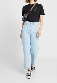Černé tričko s bílým liniovým kreslením, světle modré volné džíny a černé tenisky. Malá černá crossbody taška s hnědým popruhem.