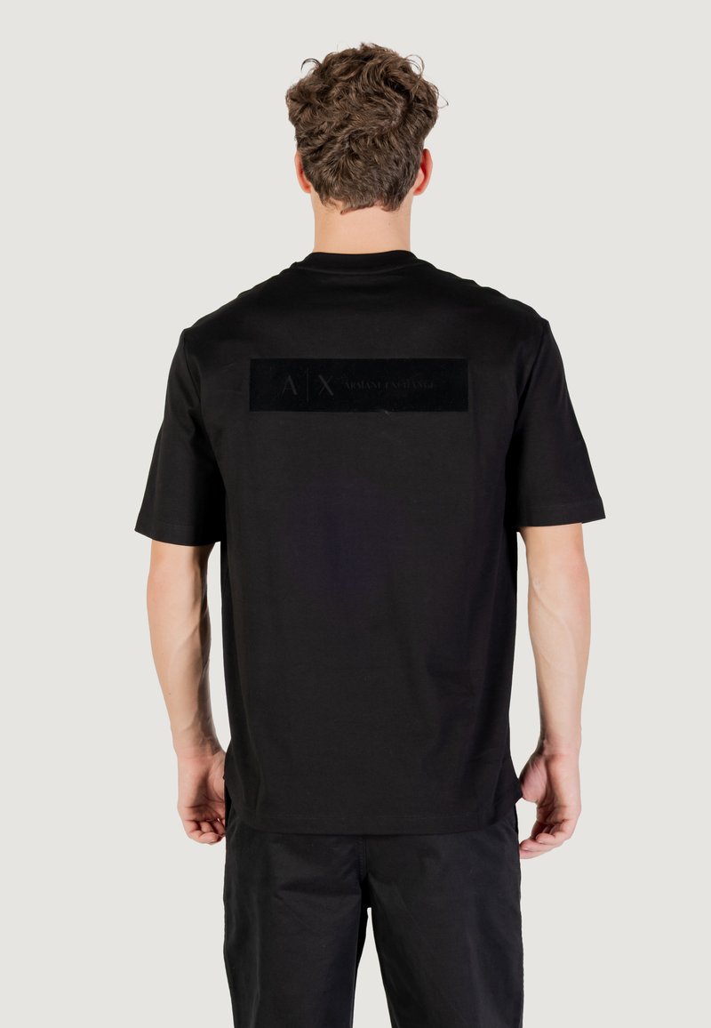 Camiseta de algodón negra con mangas cortas, que presenta un parche de logo texturizado en negro en la parte posterior y un ajuste relajado.